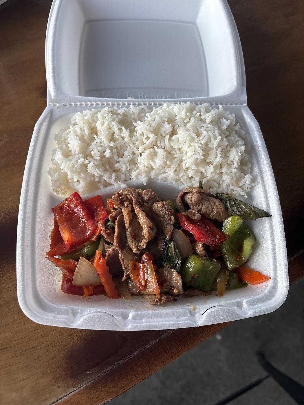 Basil chicken with peppers over rice in a takeout container