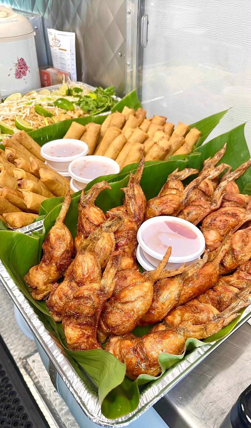 A catering tray of fried chicken pieces laid on banana leaf with cups of sauce