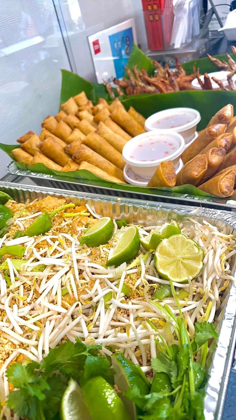 Catering trays of egg rolls with dipping sauce and pad Thai with bean sprouts and lime